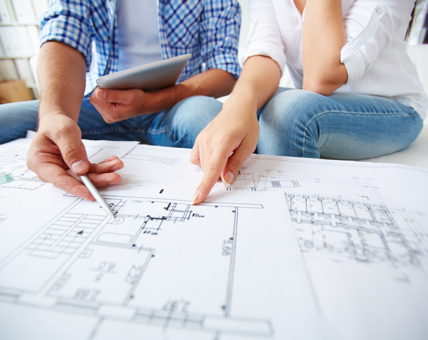 A couple reviewing floor plans with a contractor on a tablet during pre-construction