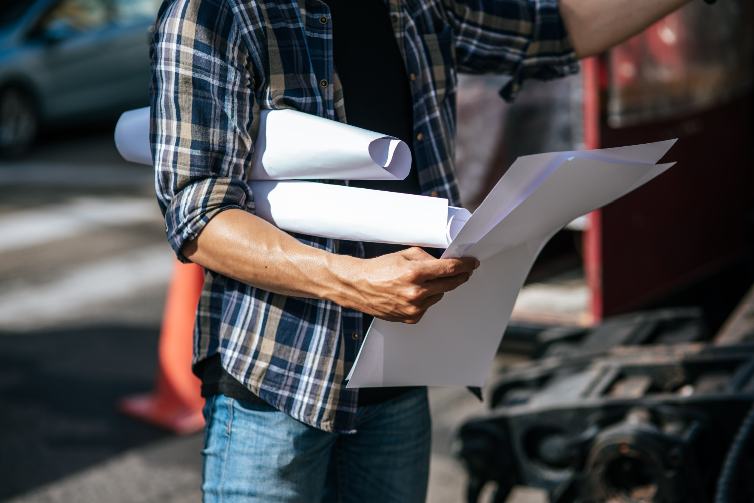 Contractor carrying rolled permit drawings and plan sheets at a job site